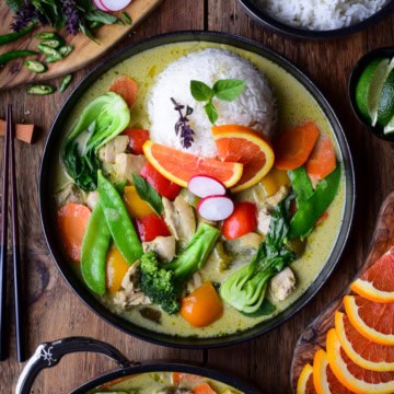A colourful and vibrant plate of Thai Green Curry Chicken & Vegetables. Served with jasmine rice, Thai basil, orange slices and green chilies.