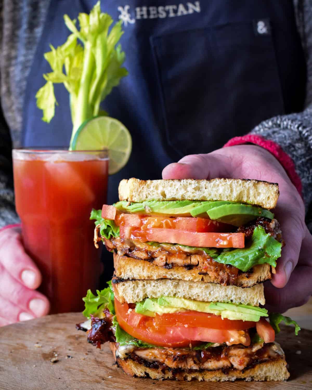 Two haves of a BBQ spicy chicken club sandwiched stacked together with a spicy Caesar cocktail.