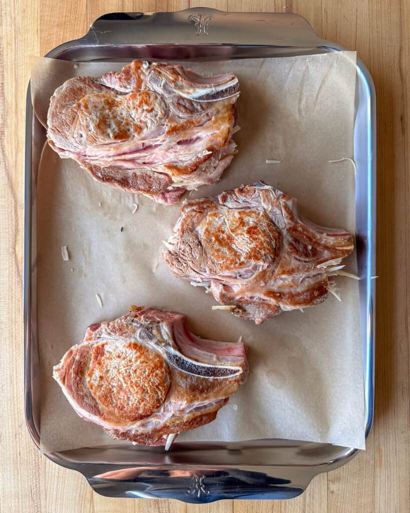 Three stuffed pork chops placed on the parchment lined sheet pan ready to go into the oven.