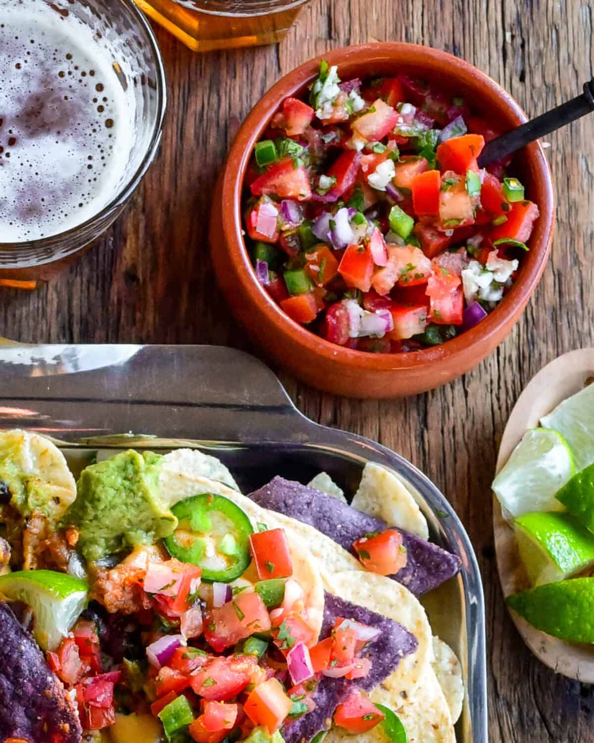 A bowl of Pico de Gallo beside a tray of nachos.