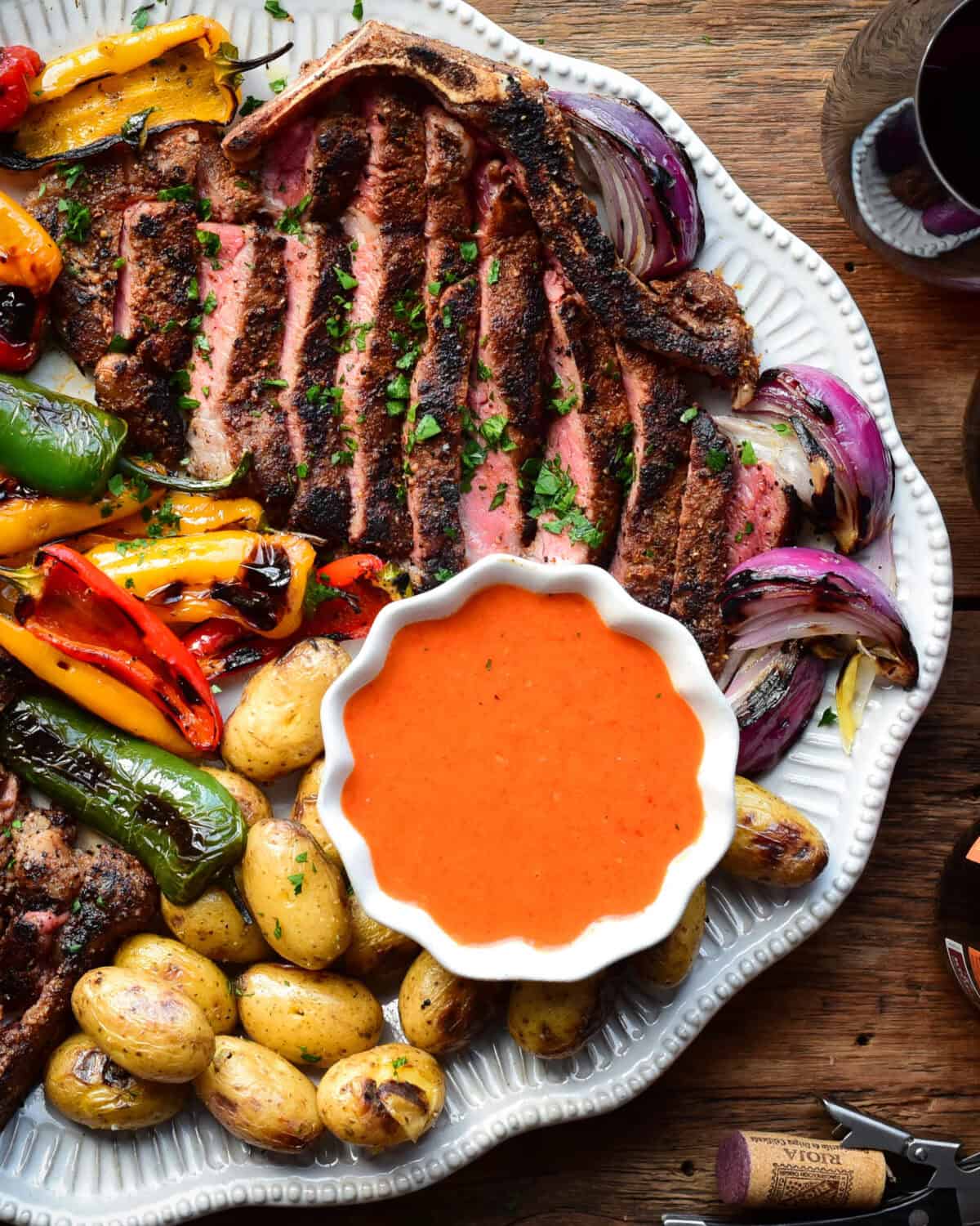 A close up of a bright orange Spanish steak sauce on a platter with steak slices and grilled vegetables.