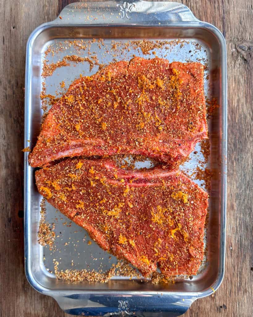 Two steaks seasoned liberally with the steak rub and orange zest.