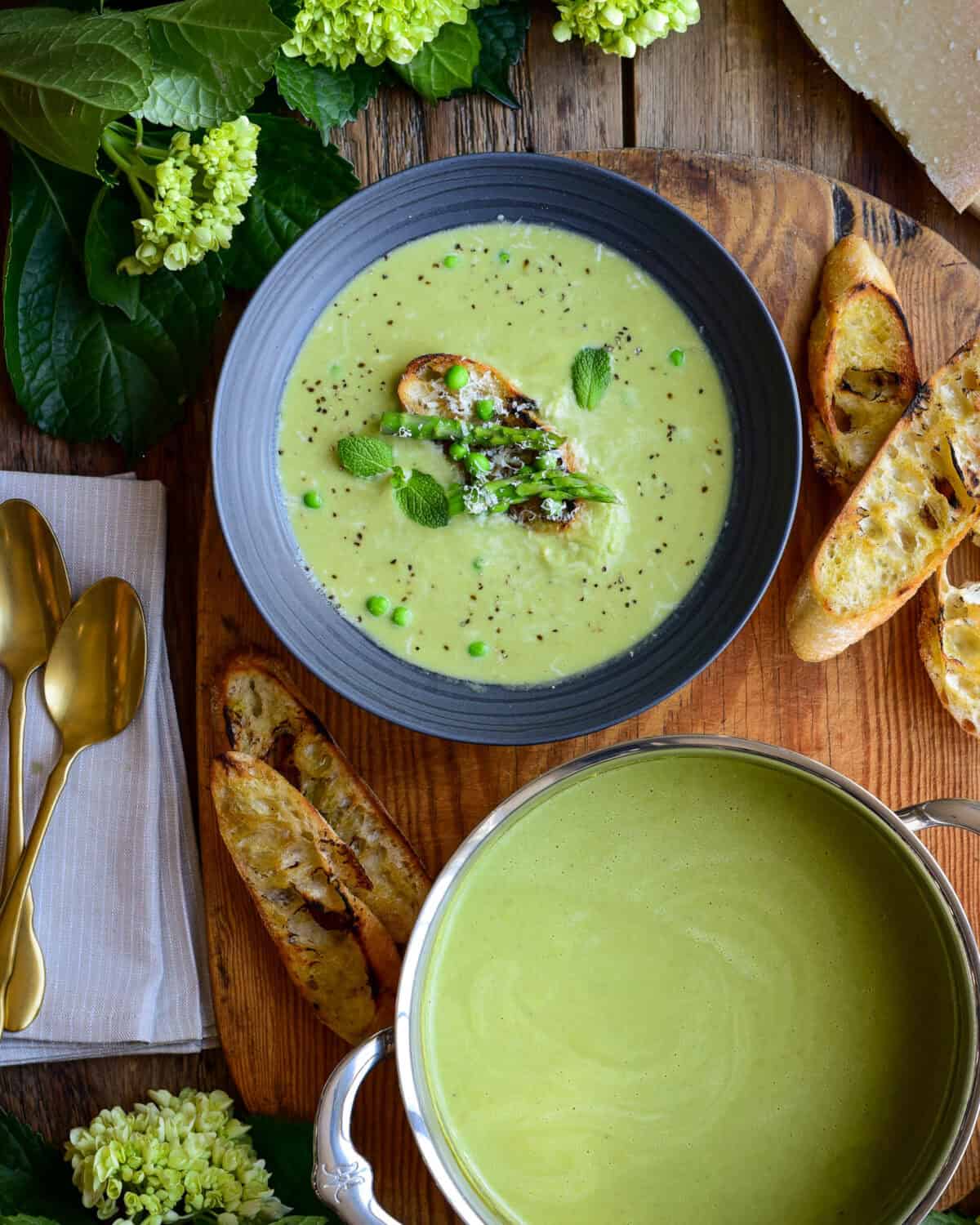 A pot and bowl of Spring Pea and Asparagus Soup served with baguette toasts.