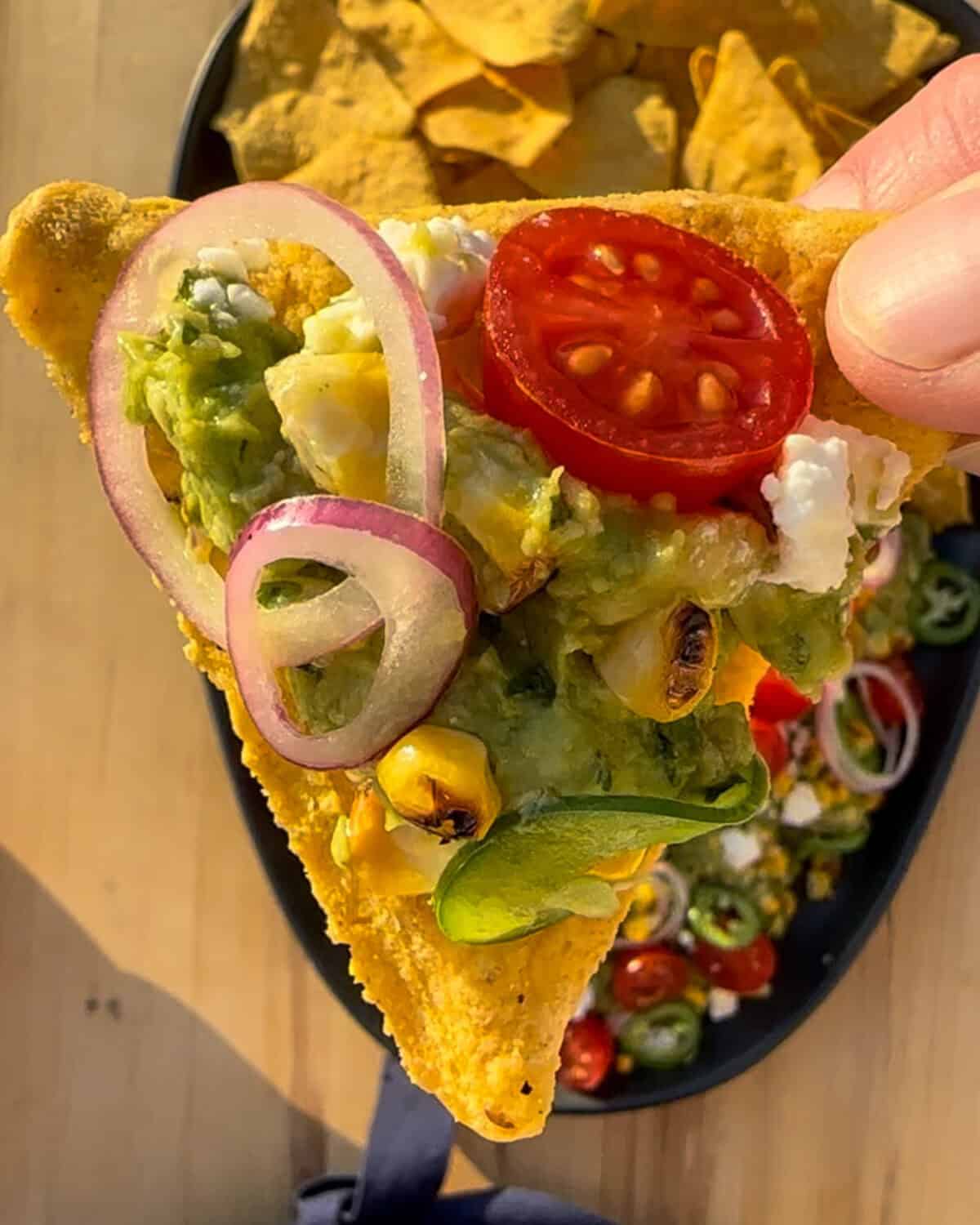 Tortilla chip with a grilled corn guacamole with onions & jalapeno slices and tomatoes.