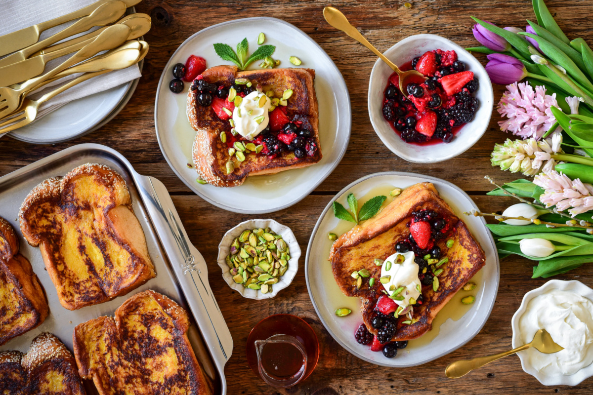 Two plates of challah French toast with mascarpone whipped cream, maserated berries and chopped pistacios.
