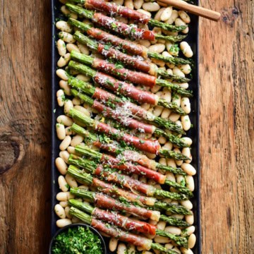A platter with Air Fryer Asparagus wrapped Prosciutto served over a bed of cannellini beans.