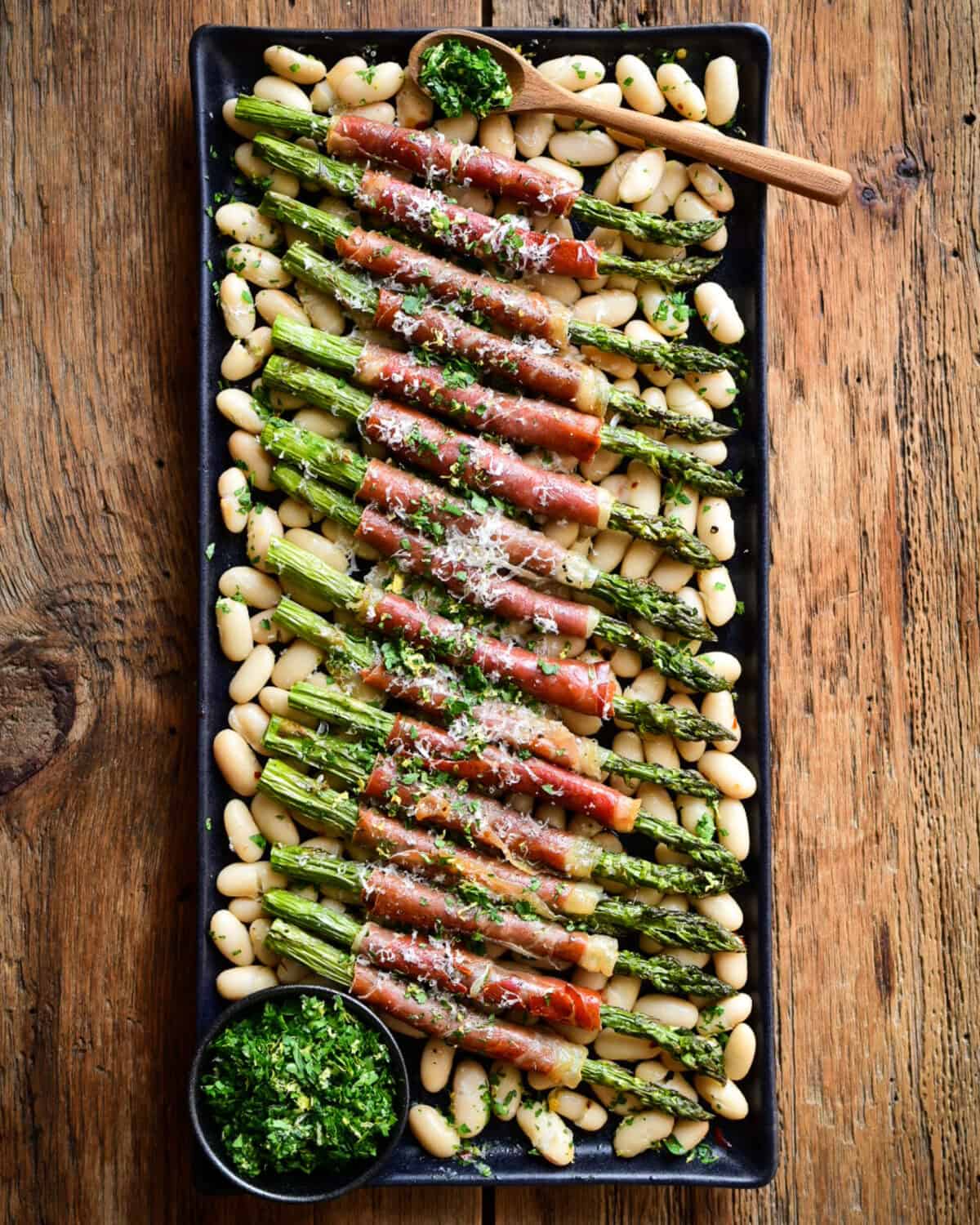 A platter with Air Fryer Asparagus wrapped with Prosciutto served over a bed of cannellini beans.