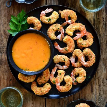 A dish of with air fryer coconut shrimp and a bowl of dipping sauce.