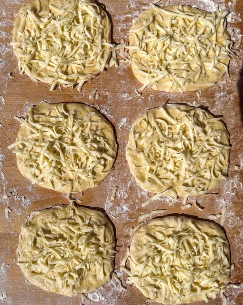 Six rolled out pizza dough brushed with olive oil and topped with shredded mozzarella.