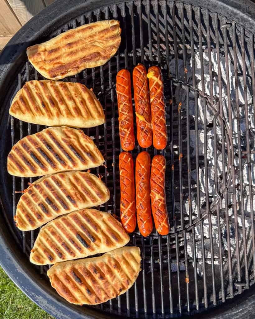 Grill marks on the pizza dough 'bun' and crosshatched smokies are cooked. Both are on the indirect side of the bbq.