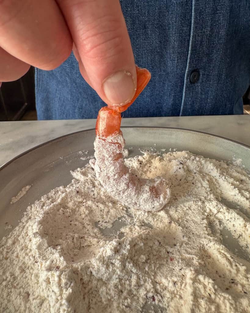 Hold the tail of the shrimp and dredge it in the flour mixture.