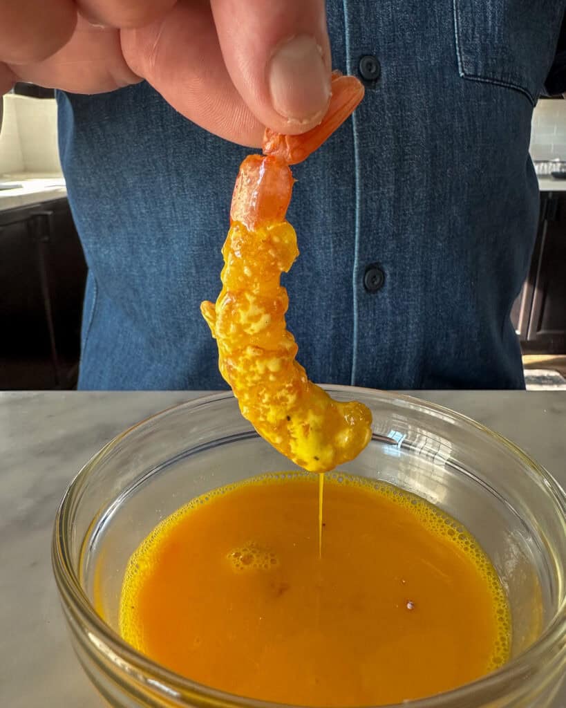 Dipping the shrimp into the beaten eggs.