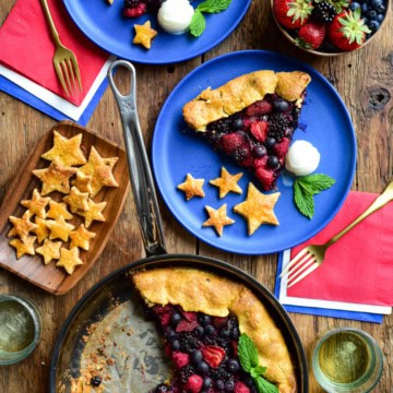 A grilled mixed berry gallet in a pan with two servings on blue plates with stars made from the crust and served with ice cream.