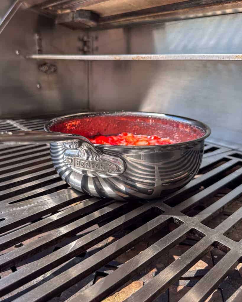 A saucepan placed on the grill to boil strawberry jam.