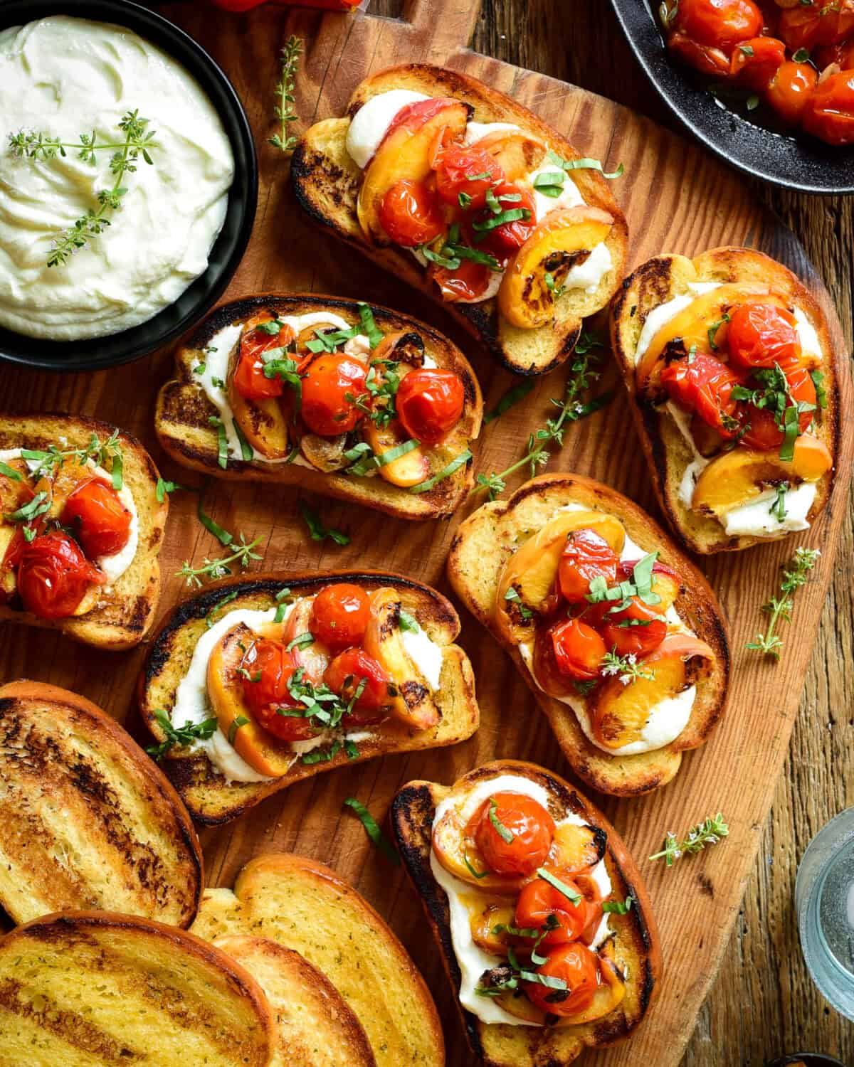 Close up of toasted garlic bread with a layer of whipped feta and topped with 3 grilled peach slices and 3 blistered tomatoes and garnished with fresh basil leaves.