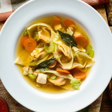 Bowl of autumn honeynut squash wonton soup featuring wontons, carrots, celery, and green onions in a clear broth, served in a white bowl on a rustic wooden table.
