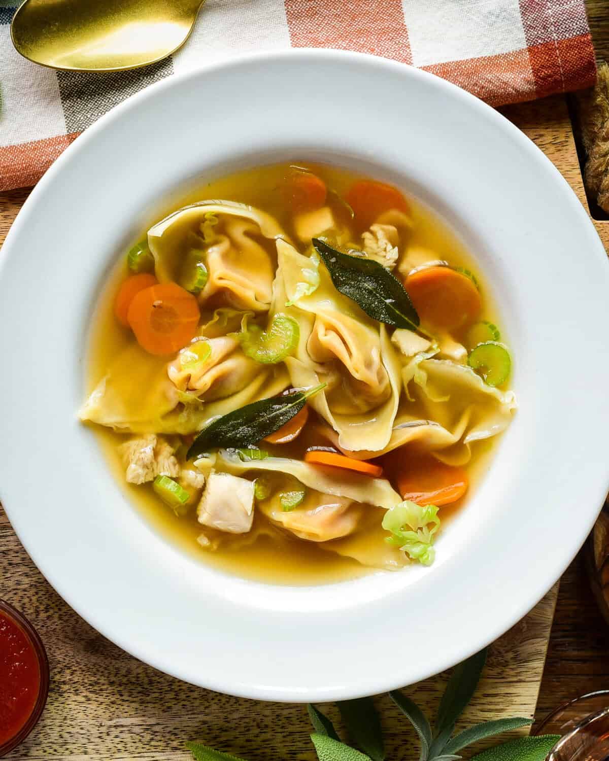 Bowl of autumn honeynut squash wonton soup featuring wontons, carrots, celery, and green onions in a clear broth, served in a white bowl on a rustic wooden table.