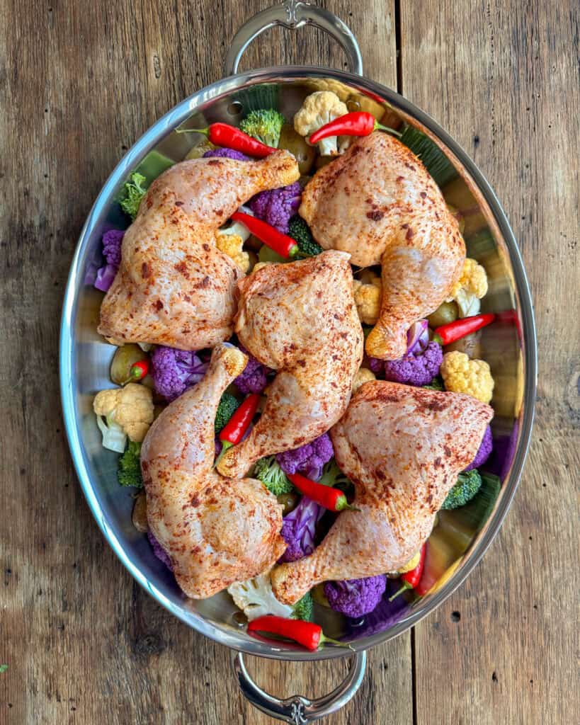 Seasoned piri piri chicken legs place on vegetables to bake.