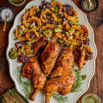 An herb butter spatchcock chicken on a platter with with roasted delicata squash and cauliflower.
