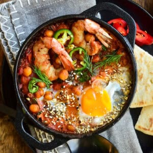 A close up of a individual shakshuka with shrimp and an egg.