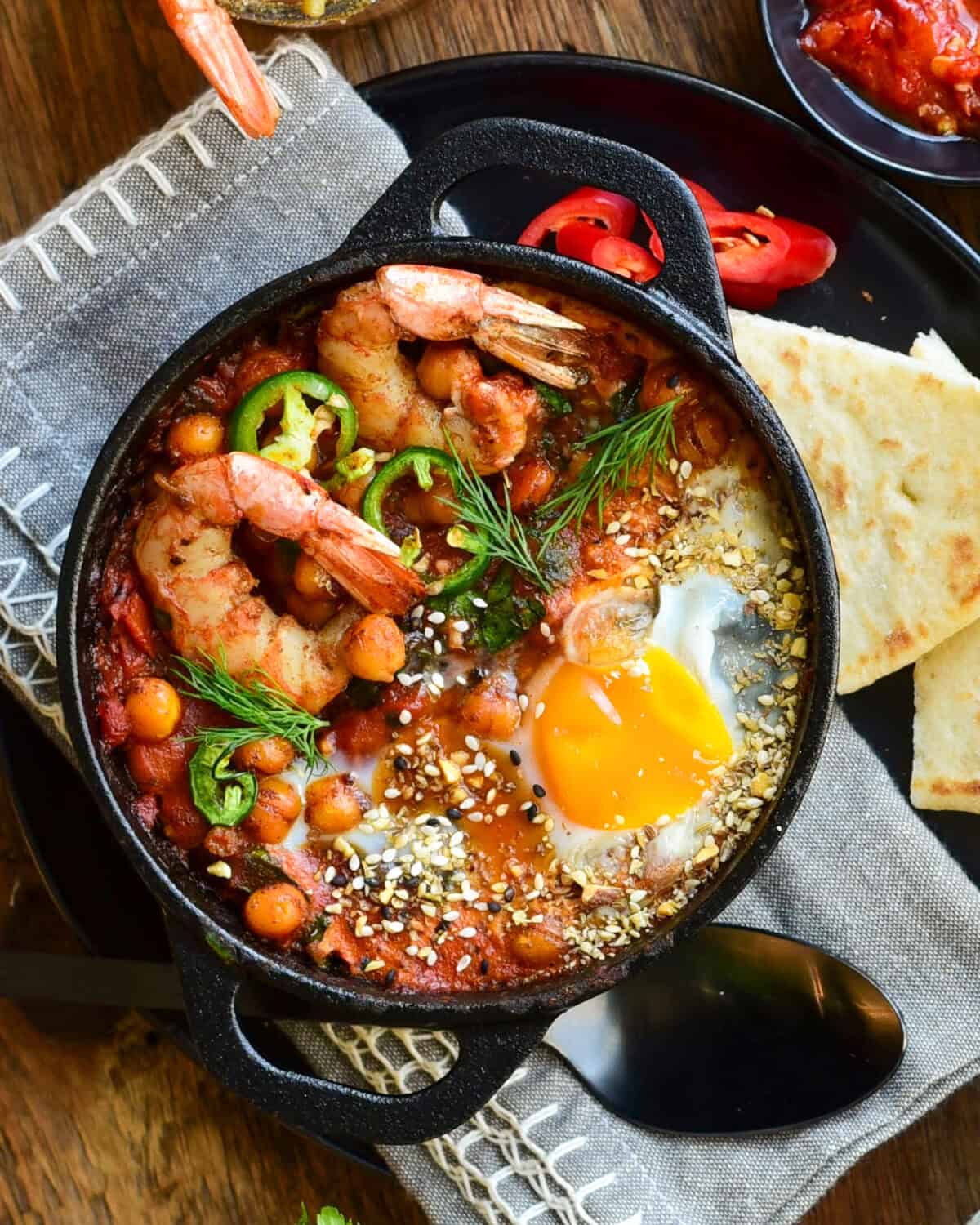 A close up of a individual shakshuka with shrimp and an egg.