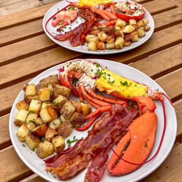 Two plates, each with a split lobster and eggs served with bacon and homefries.