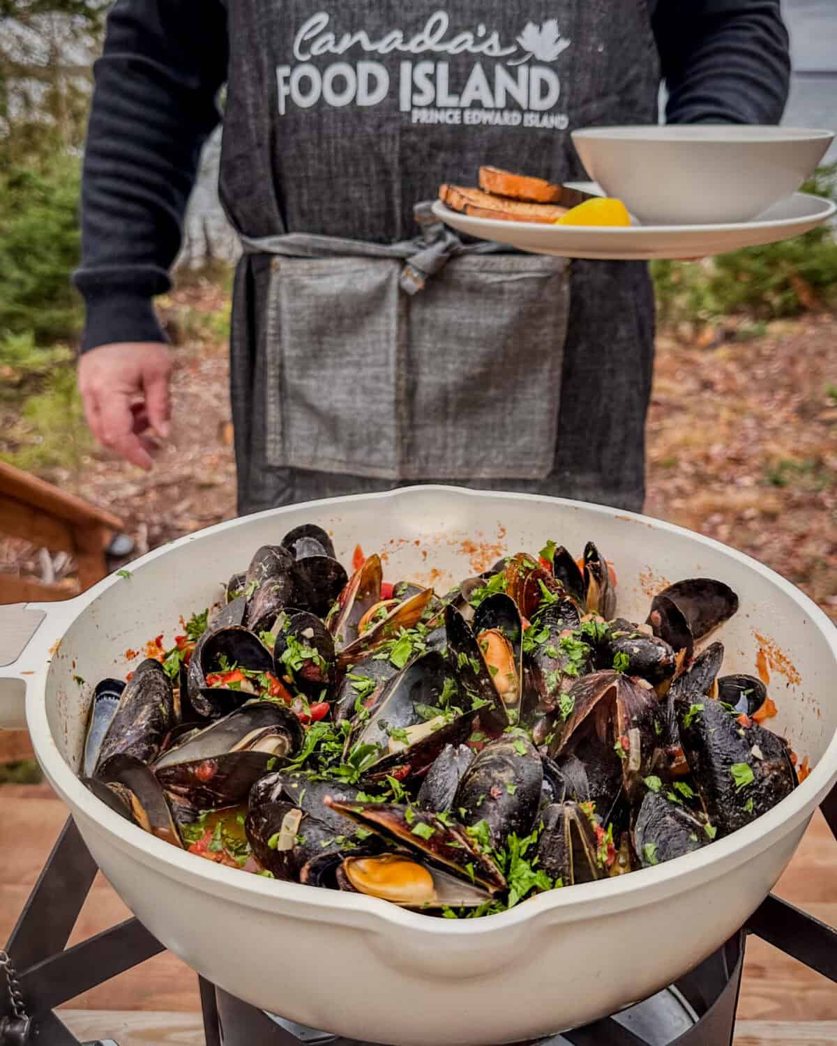 A large pot of Mussels In Spicy Tomato Broth with the chef wearing a Canada's Food Island apron.