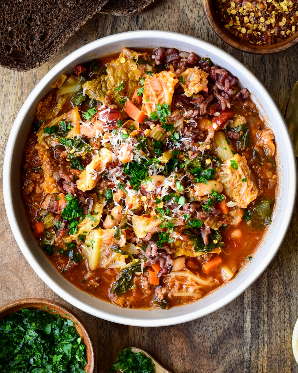A bowl of Savoy Cabbage Roll Soup with spinach and beans. Topped with chopped parsley and grated Parmesan.