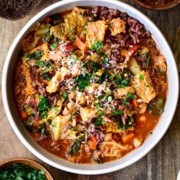 A bowl of Savoy Cabbage Roll Soup with spinach and beans. Topped with chopped parsley and grated Parmesan.
