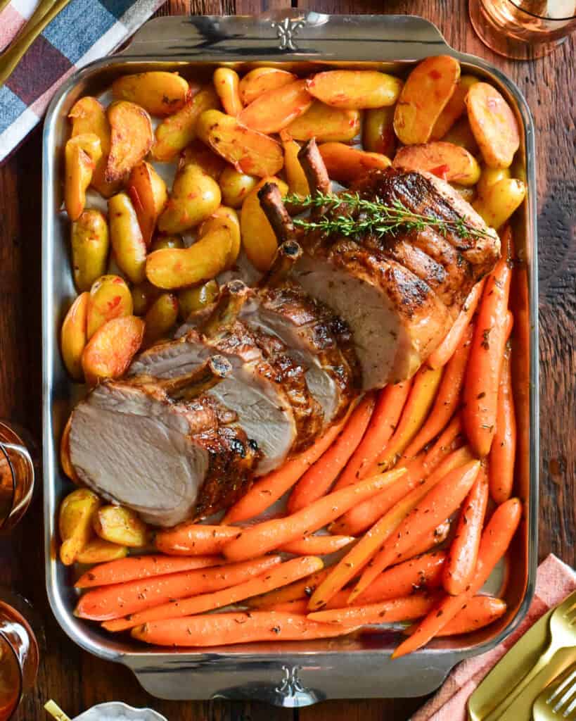 A sliced frenched bone in pork loin roast served with carrots and potatoes.