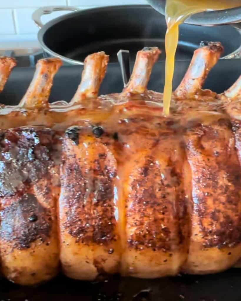 Maple Dijon glaze is being poured over a frenched bone-in rack of pork.