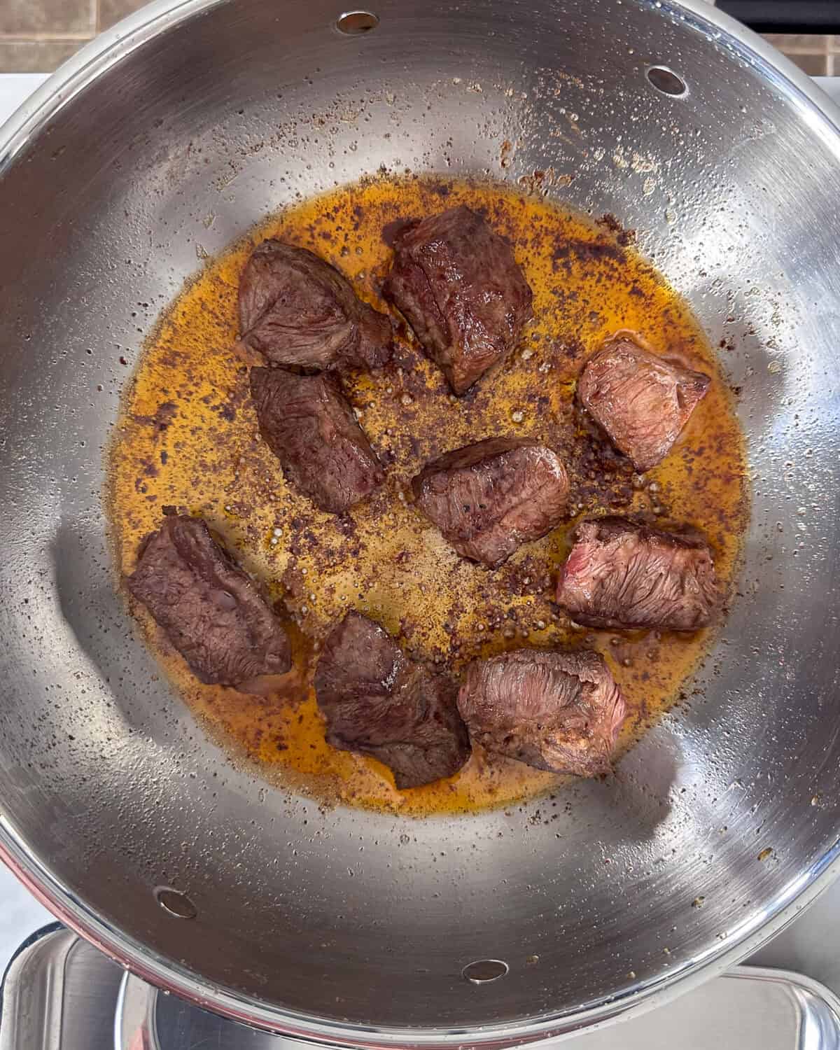 Nine seared beef cubes in a pan.