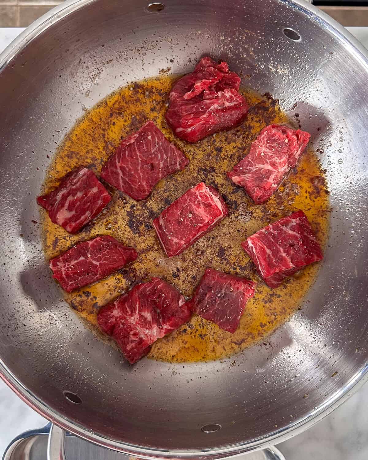 Nine pieces of beef getting seared for stew.