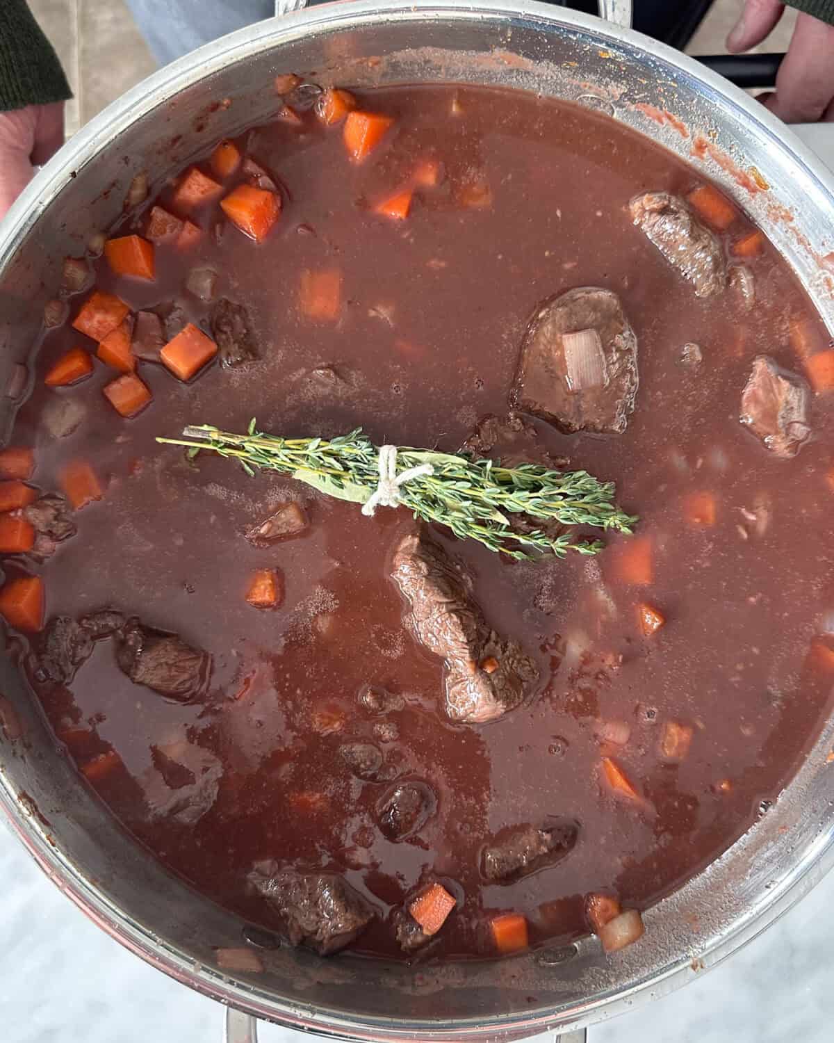 A pot of beef bourguignon with a herb bouquet about to get braised.