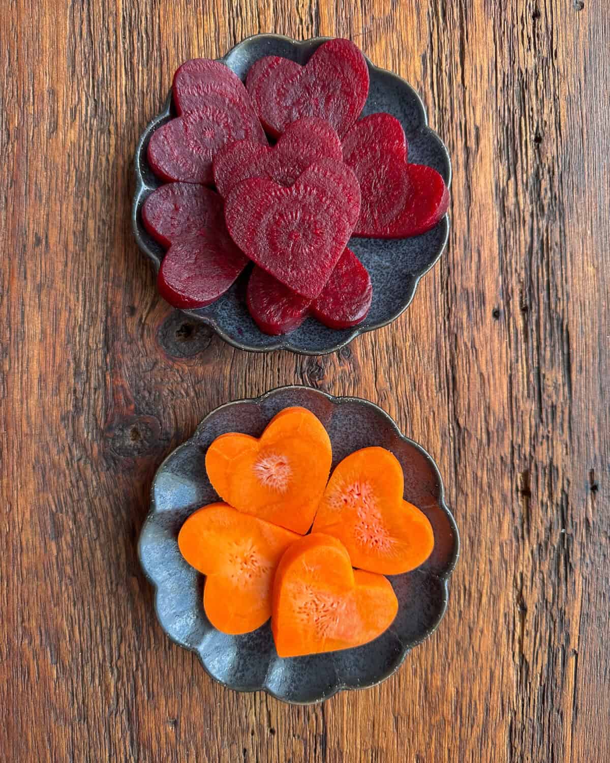 Two small black scalloped plates one with beet cut-out hearts and one with carrot cut out hearts.