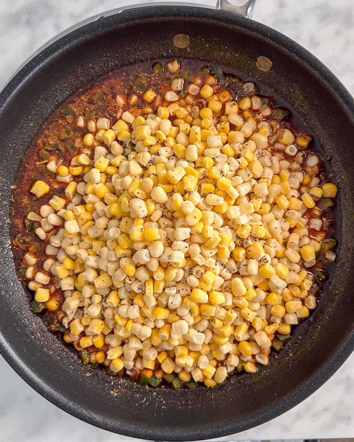 A skillet with all the ingredients for a Cajun Corn recipe about to get cooked.