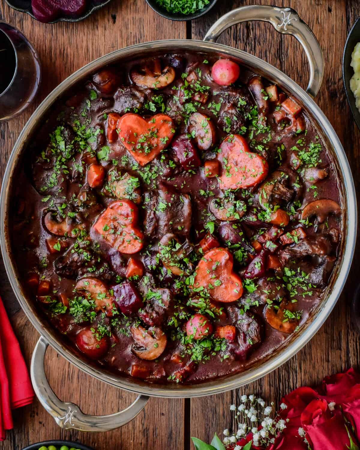 A close-up of a pot of Beef Bourguignon in a Dutch oven with root vegetables cut into hearts.
