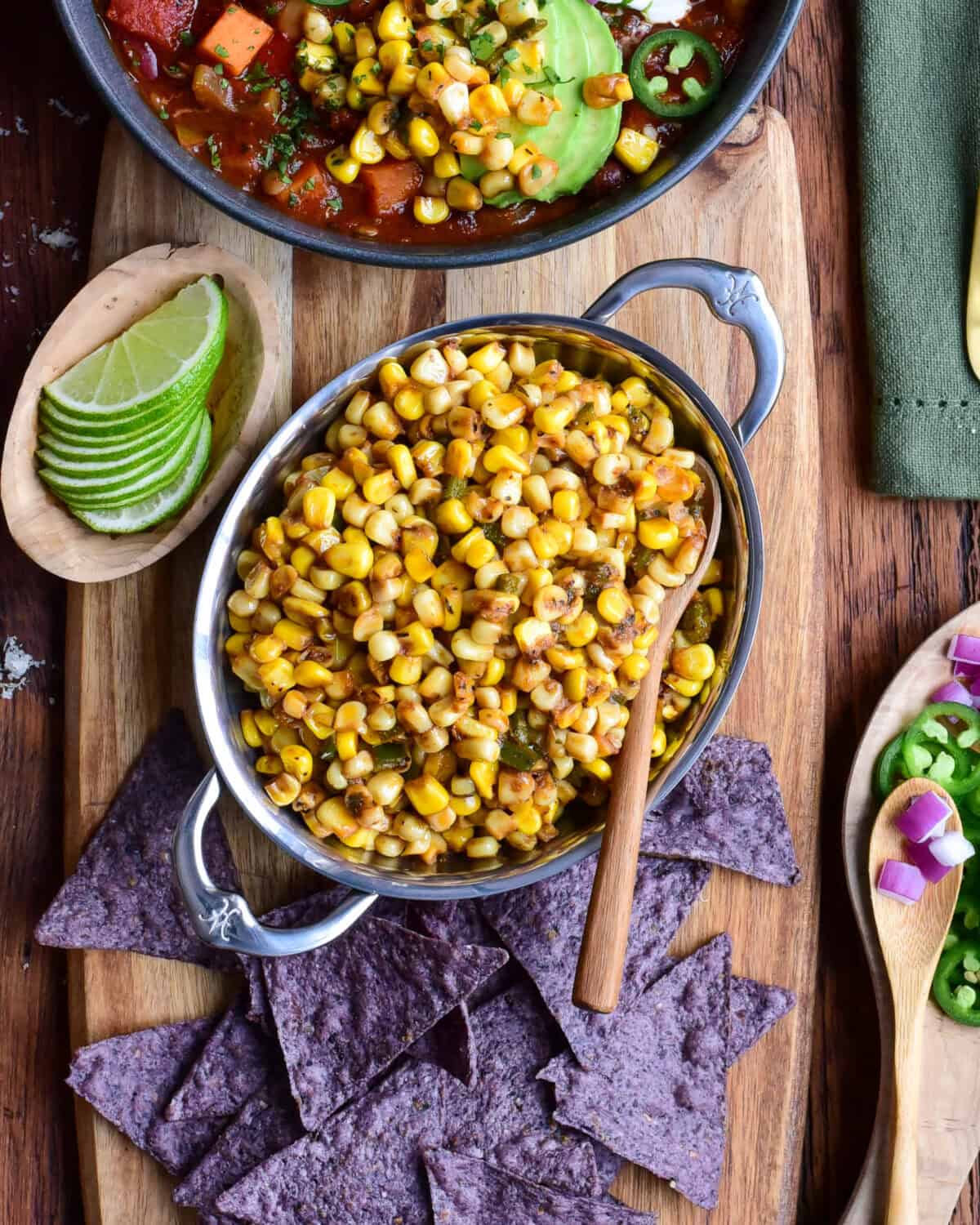 A bowl of Cajun corn served with tortilla chips, limes and chili.