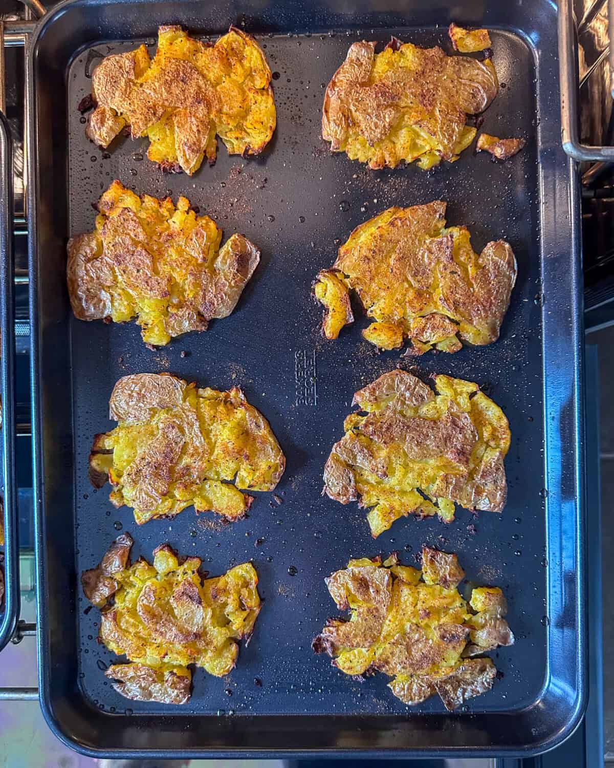 Eight baked smashed yellow potatoes on a sheet pan.