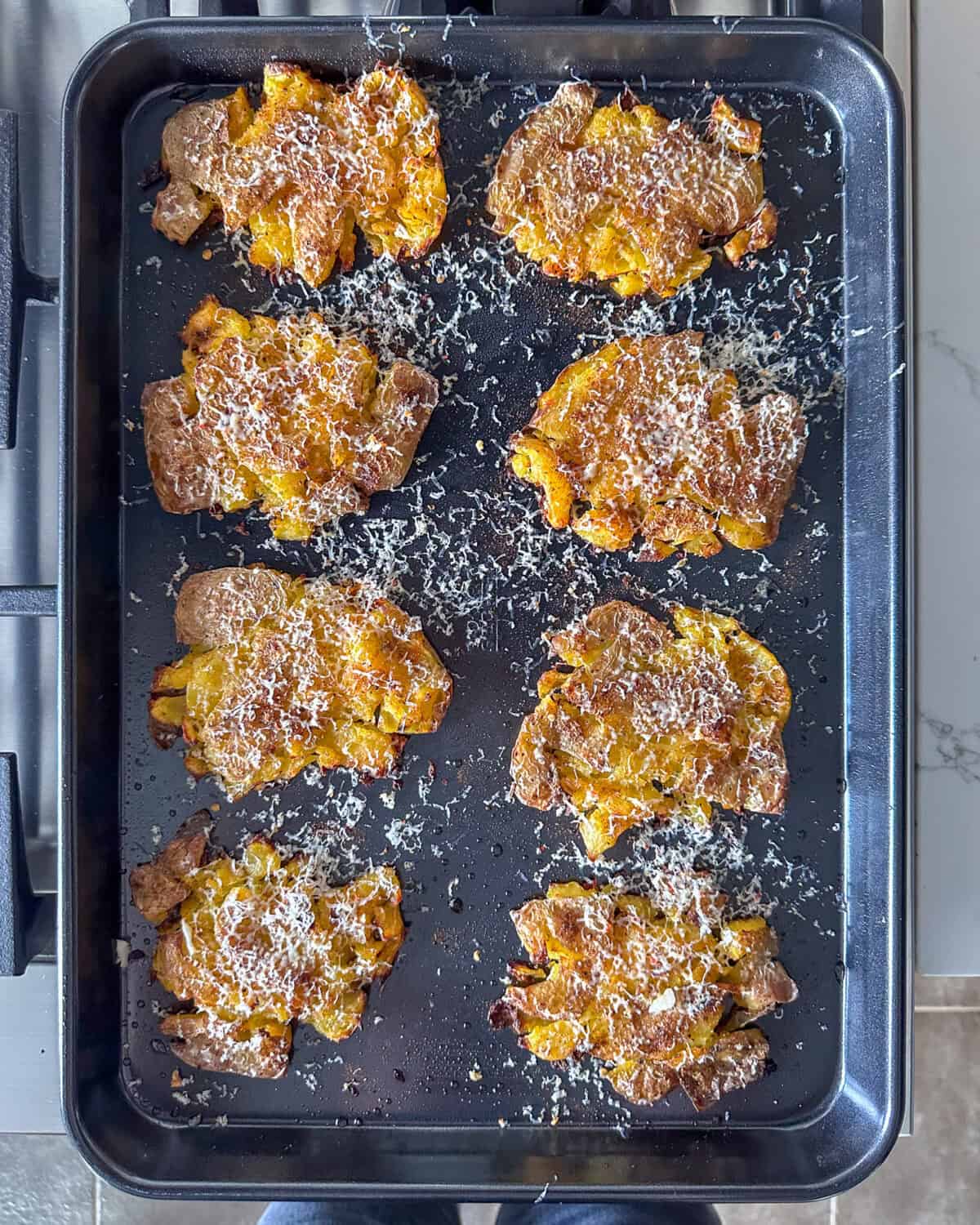 Eight baked smashed yellow potatoes on a sheet pan.