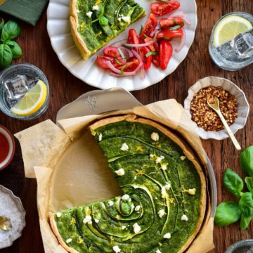 A green goddess quiche with zucchini & Feta with a piece taken out and served with a tomato salad.