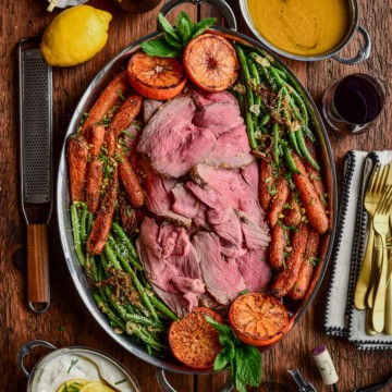A serving platter of a Charred Citrus & Turmeric Yogurt Marinated Lamb served with carrots, green beans and charred oranges.