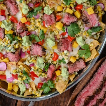 An oval platter of Carne Asada Nachos with Elote Salsa & Oaxaca Fondue served with extra steak.