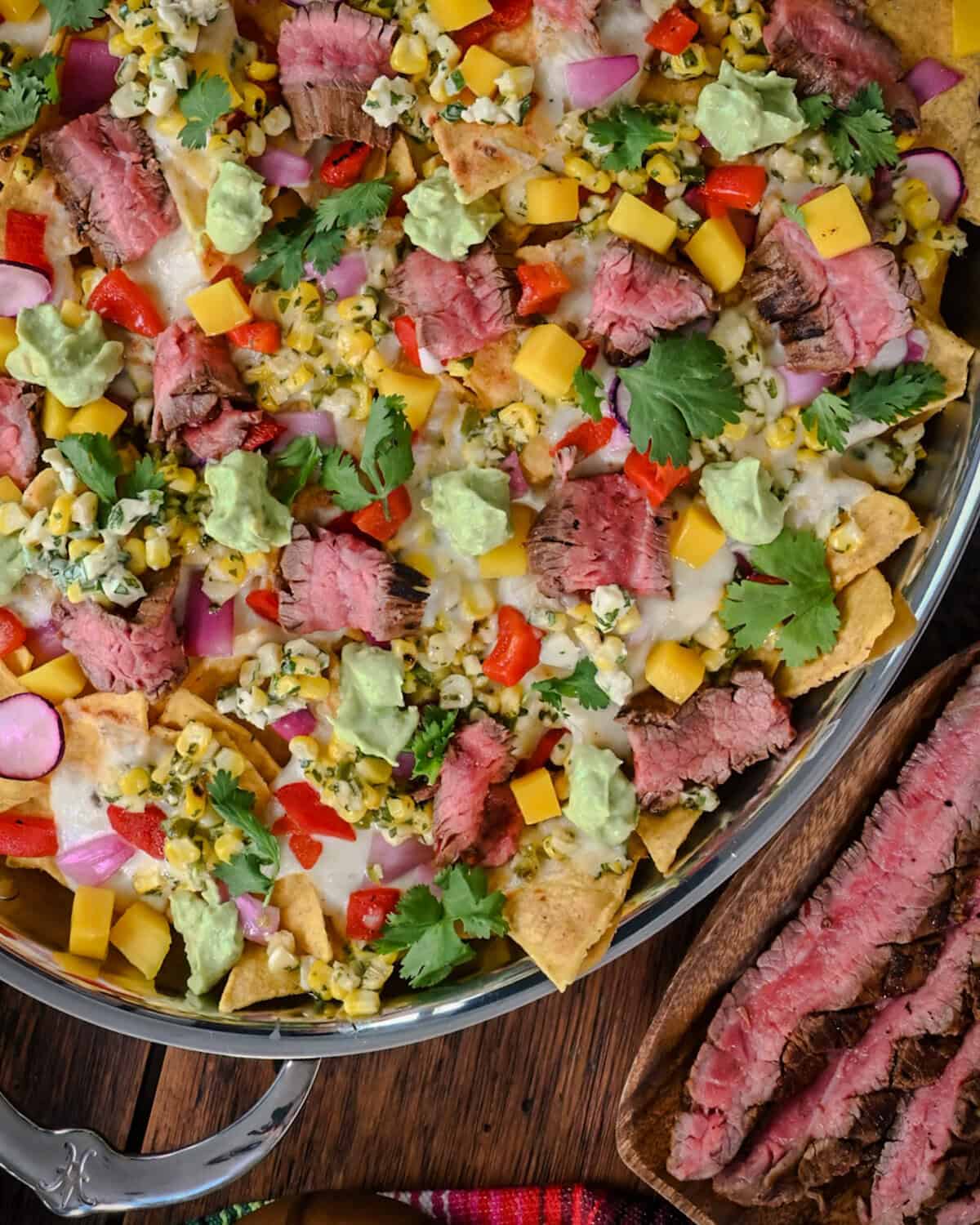 An oval platter of Carne Asada Nachos with Elote Salsa & Oaxaca Fondue served with extra steak.