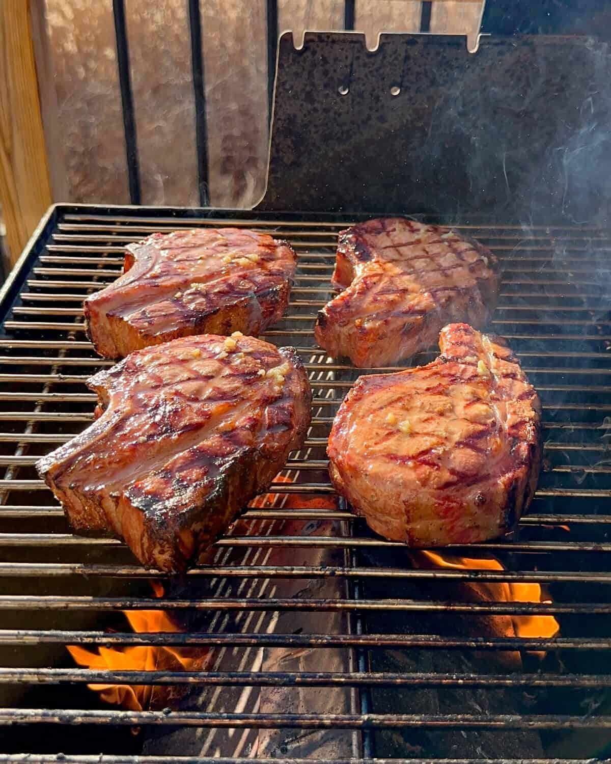Four thick-cut chops on a pellet smoker are getting seared.