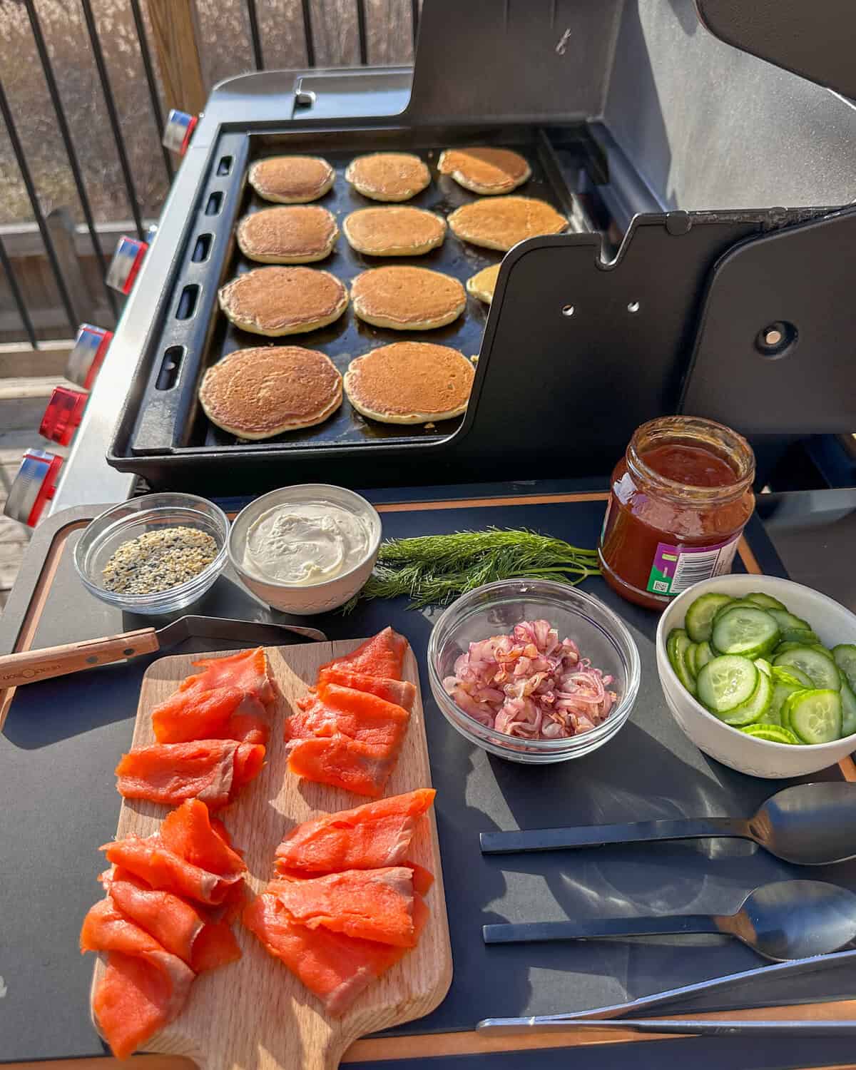 Cooked pancakes on a griddle with all the toppings for pancakes and smoked salmon.