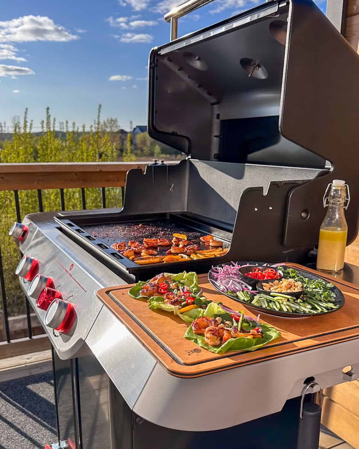 Griddled Shrimp & Charred Mango Lettuce Wraps on the Weber Searwood side table. Extra shrimp and mango are on the griddle, and a plate with extra toppings is next to the wraps.