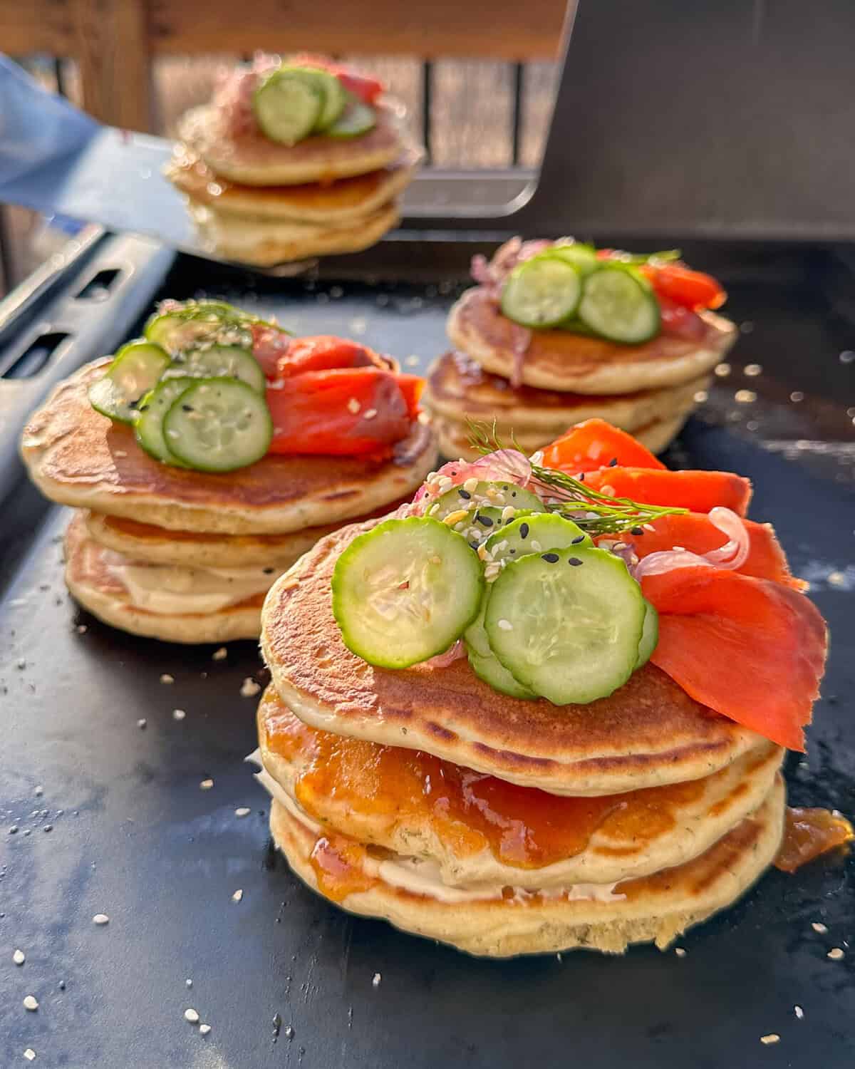 Four stacks of Lemon Dill Pancakes with Smoked Salmon and Mango Chutney on an outdoor griddle.