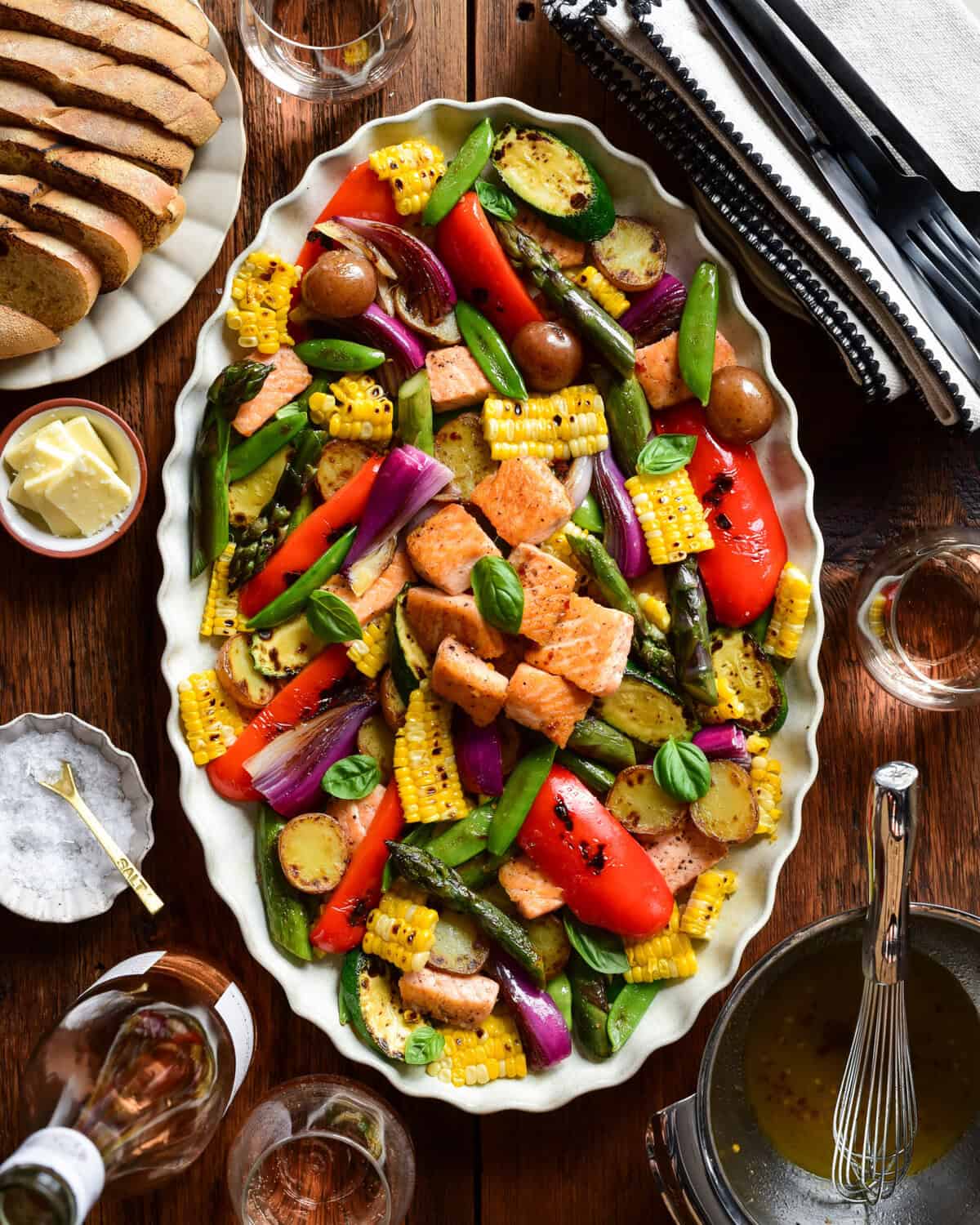 A scalloped platter with a charred corn & salmon salad, served with bread and butter, rose wine and extra dressing.