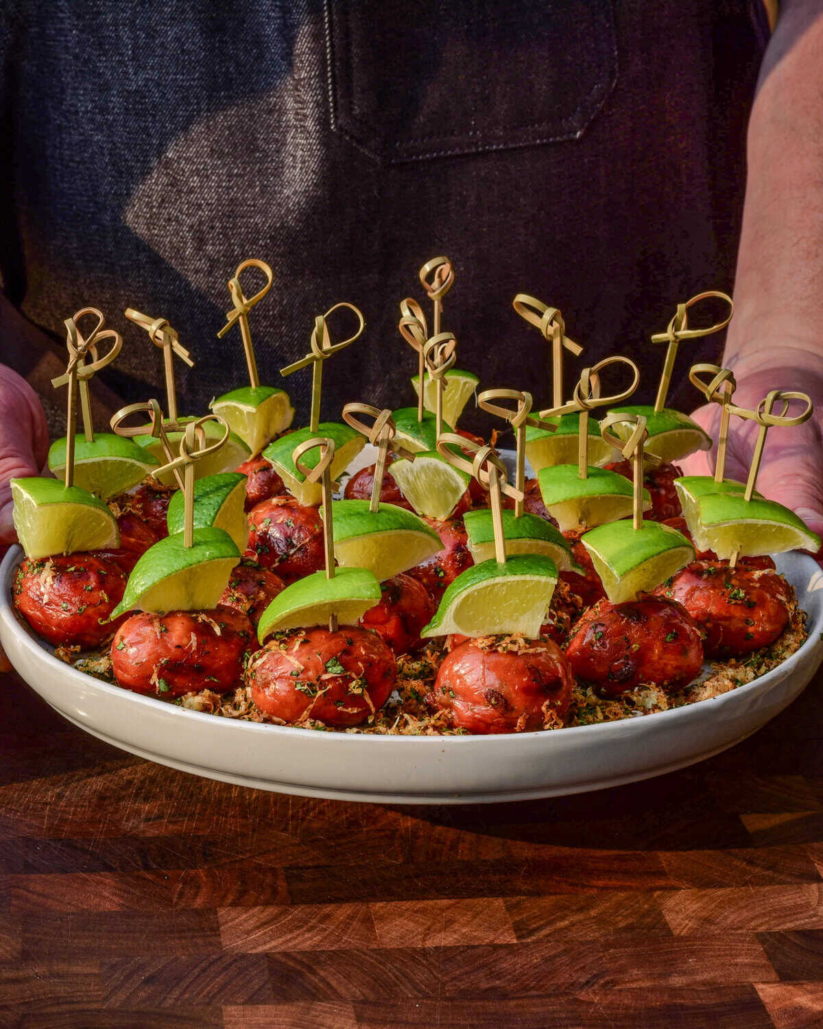 A platter of lil smokies skewered with lime wedges and coated with an elote topping.